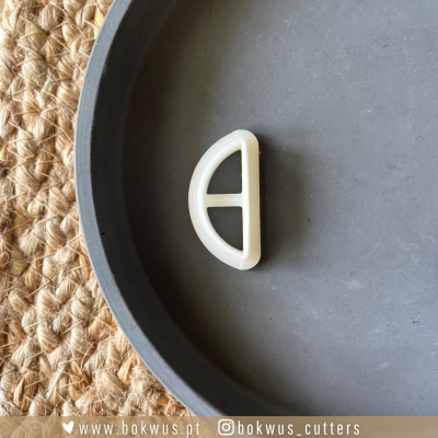 Cortador de plástico em forma de meia-lua sobre um prato cinzento e superfície de sisal