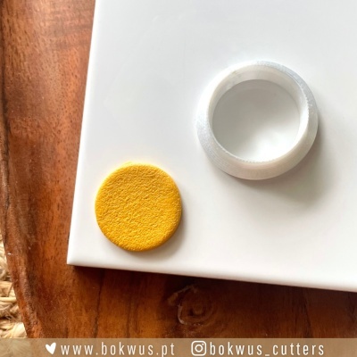 Dois objetos circulares sobre base branca, disco amarelo texturizado e anel branco liso