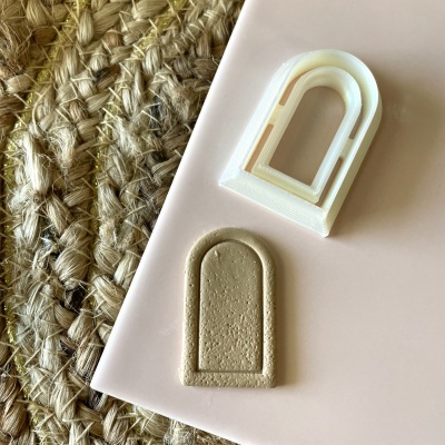 Dois objetos em forma de arco, um branco plástico e outro castanho claro, sobre superfície rosa e fundo rústico bege.