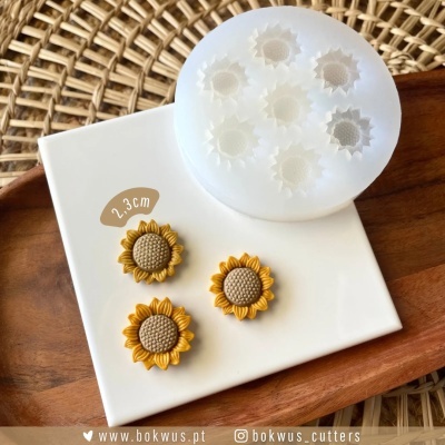 Molde silicone girassol com três peças amarelas e castanhas sobre placa branca e base madeira