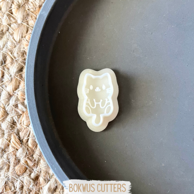 Cortador de biscoitos em forma de gato sobre prato cinzento e fundo de fibra natural