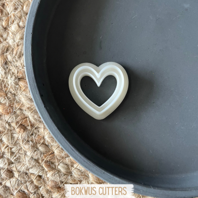 Cortador de biscoitos em forma de coração branco sobre prato preto com fundo de superfície natural entrelaçada