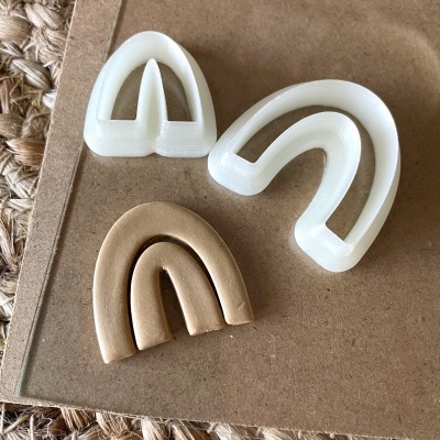 Três moldes em forma de arcos em plástico branco e castanho claro sobre cartão e superfície de corda.