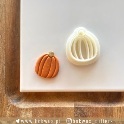 Cortador de bolachas em forma de abóbora com bolacha decorada laranja sobre placa branca