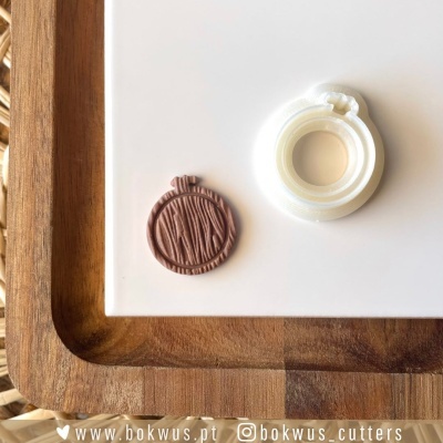 Cortador plástico branco circular e massa castanha texturizada sobre superfície branca com tabuleiro de madeira.