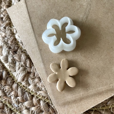 Cortador de biscoitos em forma de flor branco e peça de massa bege sobre caderno castanho sobre superfície de corda trançada