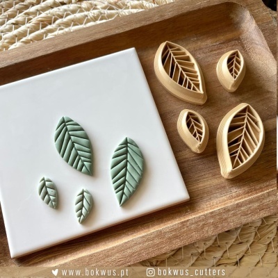 Cortadores de pastelaria em forma de folha e peças de massa verde numa bandeja de madeira.