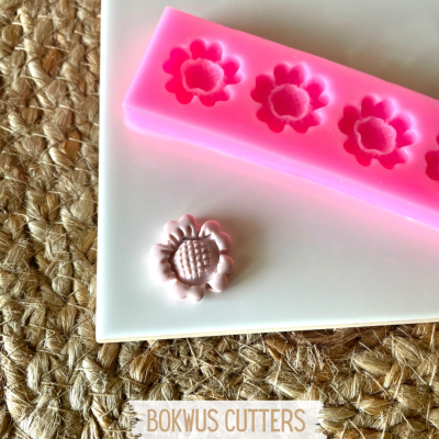 Molde de silicone rosa com cavidades em forma de flor e peça moldada branca