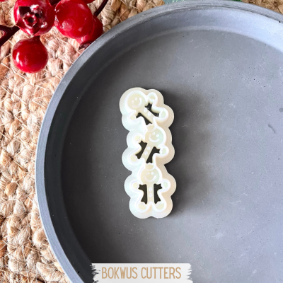 Cortador de bolacha branco com três figuras humanas sorridentes empilhadas num prato cinza