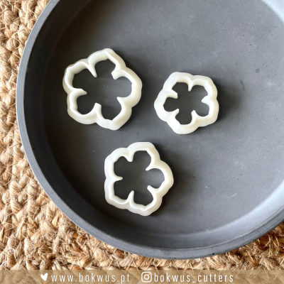 Conjunto de três cortadores de biscoito em forma de flor brancos dentro de prato cinza sobre superfície de fibra natural