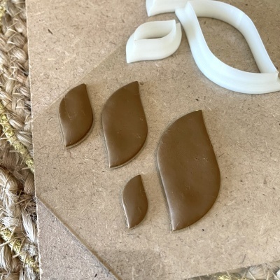 Formas de massa castanha em formato de folha sobre superfície de madeira com objeto branco em forma de folha