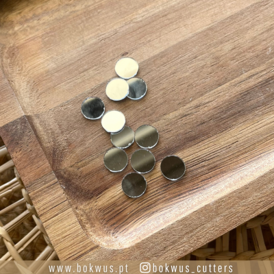 Botões prateados redondos numa bandeja de madeira sobre fundo de vime