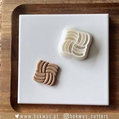 Dois cortadores de massa entrelaçados, branco e marrom claro, sobre placa branca e bandeja de madeira.