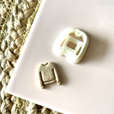 Moldador branco e mini camisola bege sobre mesa rosada e tecido entrelaçado.