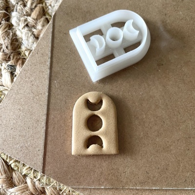 Molde branco de plástico e peça moldada bege com formas de luas sobre madeira