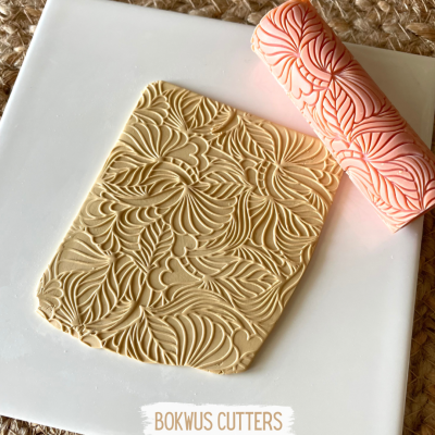 Rolo de massa cor de salmão com padrão de folhas e massa estampada em branco