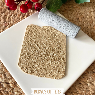 Rolo de textura para massa com padrão de flocos de neve sobre superfície branca e tape de fibras