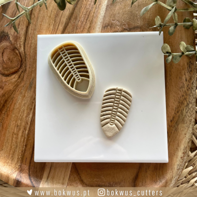 Cortador de plástico para bolachas em forma de folha com textura, colocado sobre azulejo branco em tabuleiro de madeira