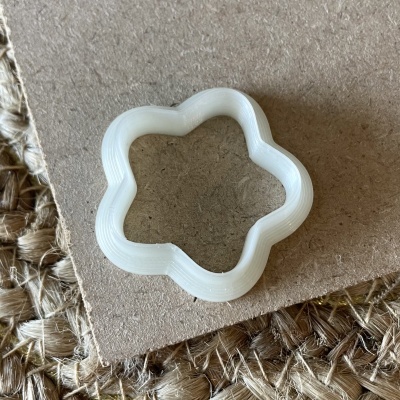 Cortador de biscoitos branco em forma de flor sobre cartão e tapete natural