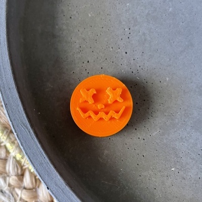 Botão laranja com rosto de abóbora sobre superfície cinzenta e tecido trançado
