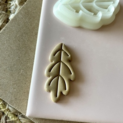 Cortador de massa branco em forma de folha com massa bege cortada ao lado sobre superfície rosa