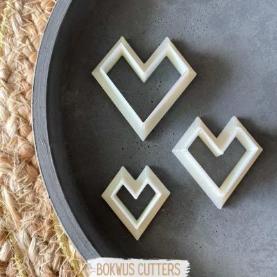 Três cortadores de massa geométricos brancos em forma de coração sobre prato cinza e tecido trançado