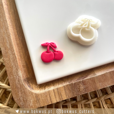 Cortadores de massa em forma de cerejas de cor vermelha e branca sobre placa branca em bandeja de madeira.