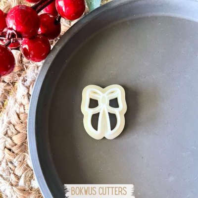 Cortador de biscoitos em forma de laço sobre prato cinza com bagas vermelhas ao lado
