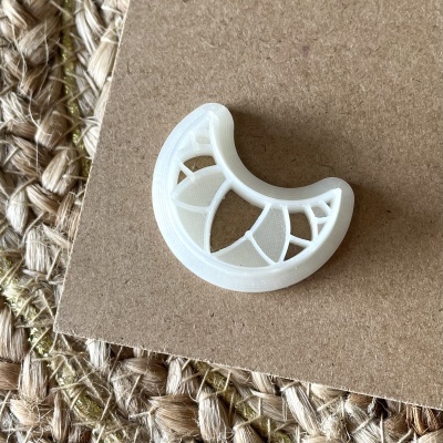 Peça decorativa branca meia-lua em plástico sobre papel castanho e tapete de ráfia