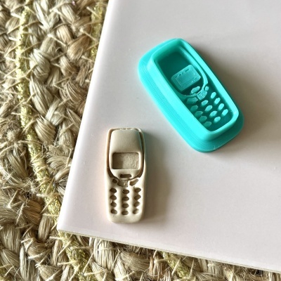 Moldes de silicone azul e branco em forma de telemóvel antigo sobre superfícies branca e trançada