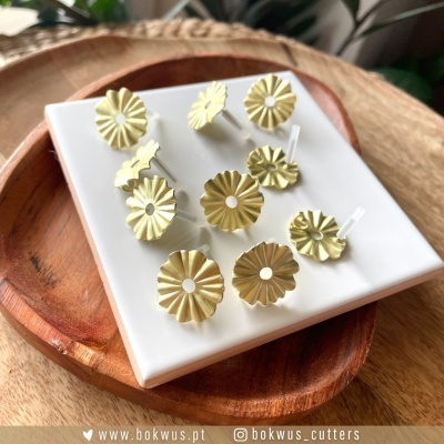 Conjunto de cortantes metálicos dourados em formato de flores sobre prato branco e base de madeira.