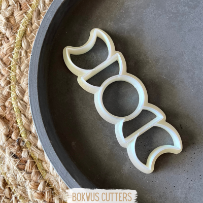 Cortador de bolachas em forma de fases da lua dentro de frigideira preta sobre superfície trançada de palha