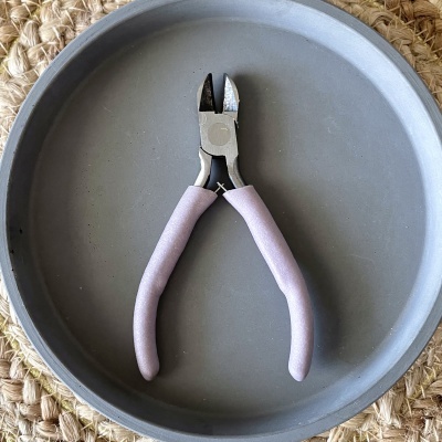 Alicate de corte lilás com cabos revestidos, em bandeja cinza sobre superfície de corda