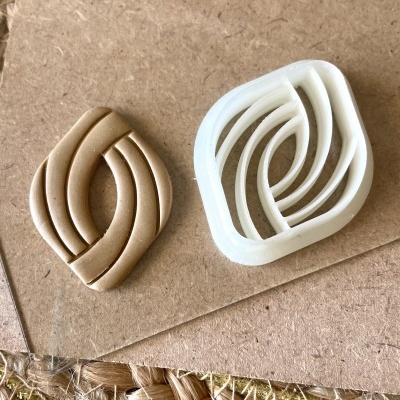 Cortador de massa branco e peça de massa marrom claro com padrão geométrico curvo sobre cartão castanho