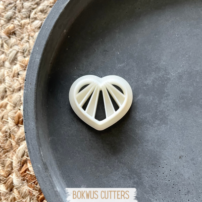 Cortador de pastelaria em forma de coração branco com divisões internas, sobre base preta e tapete de fibras