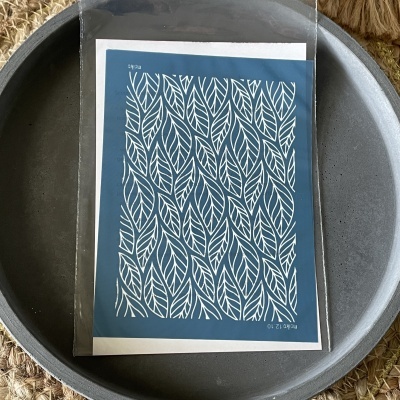 Folha azul com padrão branco de folhas embalada em plástico sobre uma bandeja cinzenta