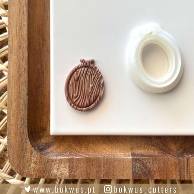 Dois cortadores de bolacha, um castanho texturizado redondo e um branco oval liso, sobre tábua de madeira e superfície branca