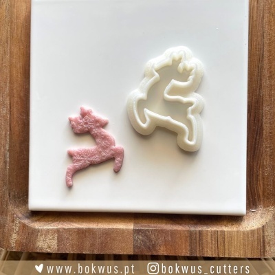 dois cortadores de massa em forma de unicórnio, um branco e outro cor-de-rosa, sobre placa branca com moldura de madeira