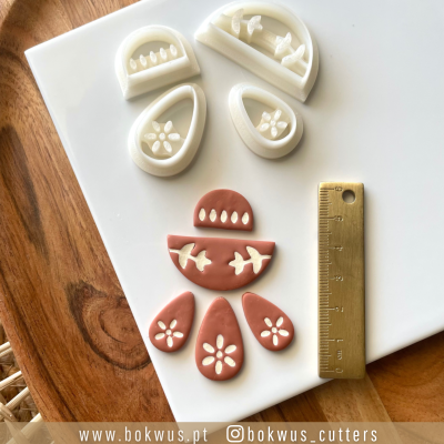 Cortadores florais e em gotas em plástico branco e terracota com régua dourada sobre base branca