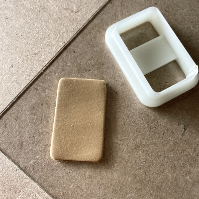 Pedaço retangular de espumilha bege e peça de plástico branca retangular sobre superfície de madeira.