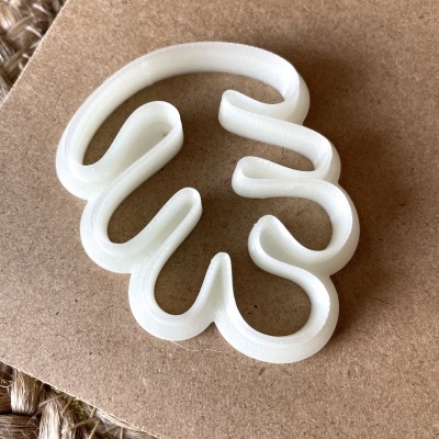 Objecto branco de plástico com design ondulado sobre fundo castanho e superfície trançada