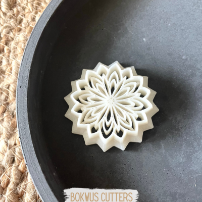 Cortante de massa branco em forma de flor numa superfície preta com tapete de fibras naturais ao lado