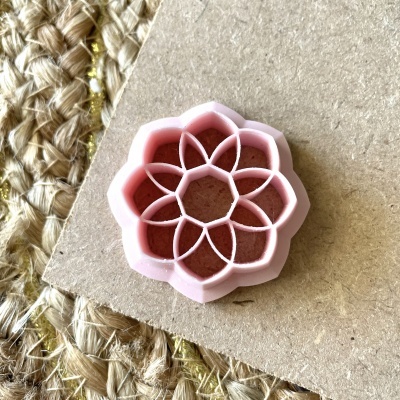 Cortador de massa ou biscoitos rosa com formato floral geométrico sobre cartão castanho