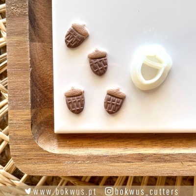 Cortadores de bolachas e bolachas em forma de bolota de chocolate sobre bandeja de madeira.