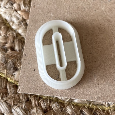 Peça de plástico oval branca com fenda, sobre cartão castanho e tecido texturizado