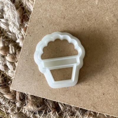 Cortante branco em forma de vaso de flores sobre superfície castanha e tecido natural