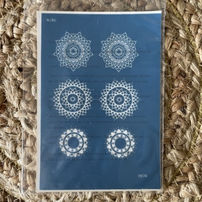 Papel azul com seis desenhos de mandalas brancas sobre superfície de corda entrelaçada.