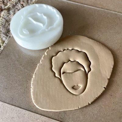 Carimbo branco com padrão de rosto estilizado ao lado de impressão em massa bege