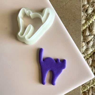 Dois cortadores de biscoitos em forma de gato, um branco e outro roxo, sobre um prato branco e fundo rústico