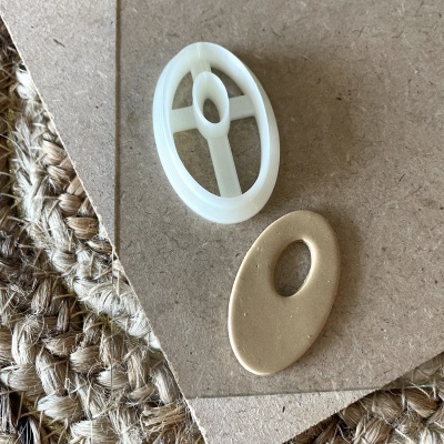 Peças ovais branca de plástico e dourada metálica em cartão castanho sobre tapete de fibras naturais